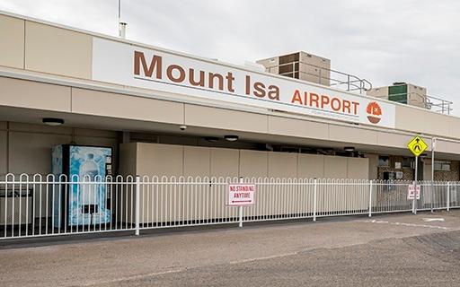 Exterior of Mount Isa Airport with signage, white fencing, and a “No Standing Anytime” sign under a cloudy sky.
