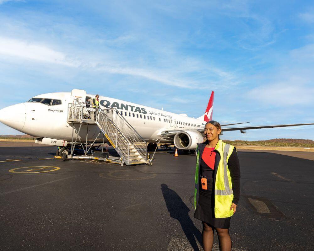 Qantas aircraft on the tarmac at Mount Isa Airport with portable stairs attached and ground staff in high-visibility vest nearby.