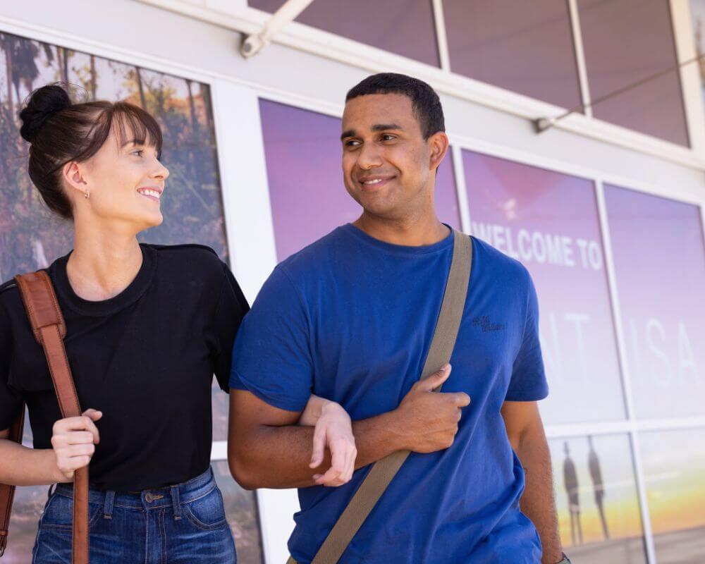 Two people walking outside Mount Isa Airport, engaged in conversation near signage that reads “Welcome to Mount ISA.