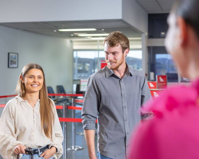 Two people at an airport check-in counter, with a staff member assisting from behind the desk.