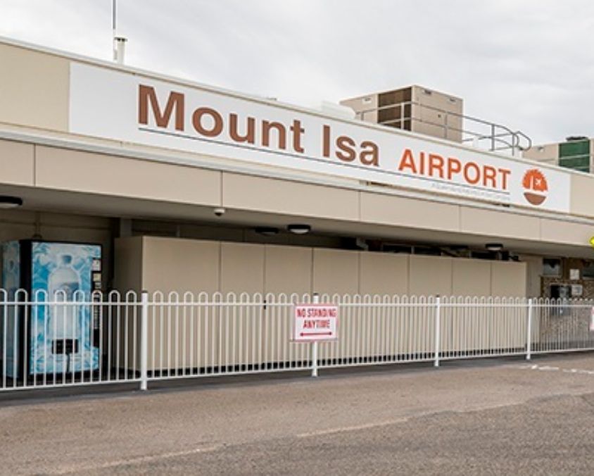 Exterior of Mount Isa Airport with signage, white fencing, and a “No Standing Anytime” sign under a cloudy sky.